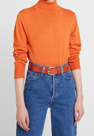 Personne portant un col roulé orange à manches longues, rentré dans un jean bleu taille haute avec une ceinture orange texturée et une boucle dorée.