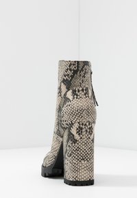 Bottine à effet peau de serpent en beige et noir, dotée d'un talon épais et d'une surface texturée. Détail de fermeture éclair au dos avec une semelle en caoutchouc robuste.