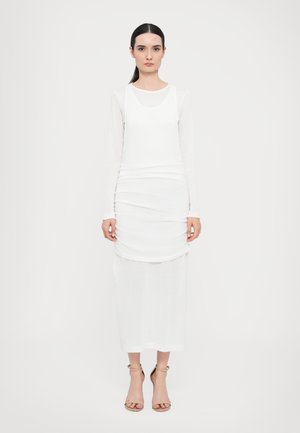 Witte lange mouw jurk met gelaagd ontwerp; heeft een ronde halslijn en rechte snit. Model draagt sandalen in neutrale tinten. Eenvoudige textuur.