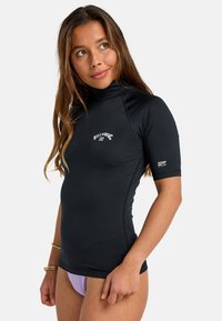 Svart kortärmad rash guard i stretchigt material, med hög krage och logga på bröstet; figurnära silhuett med platta sömmar.