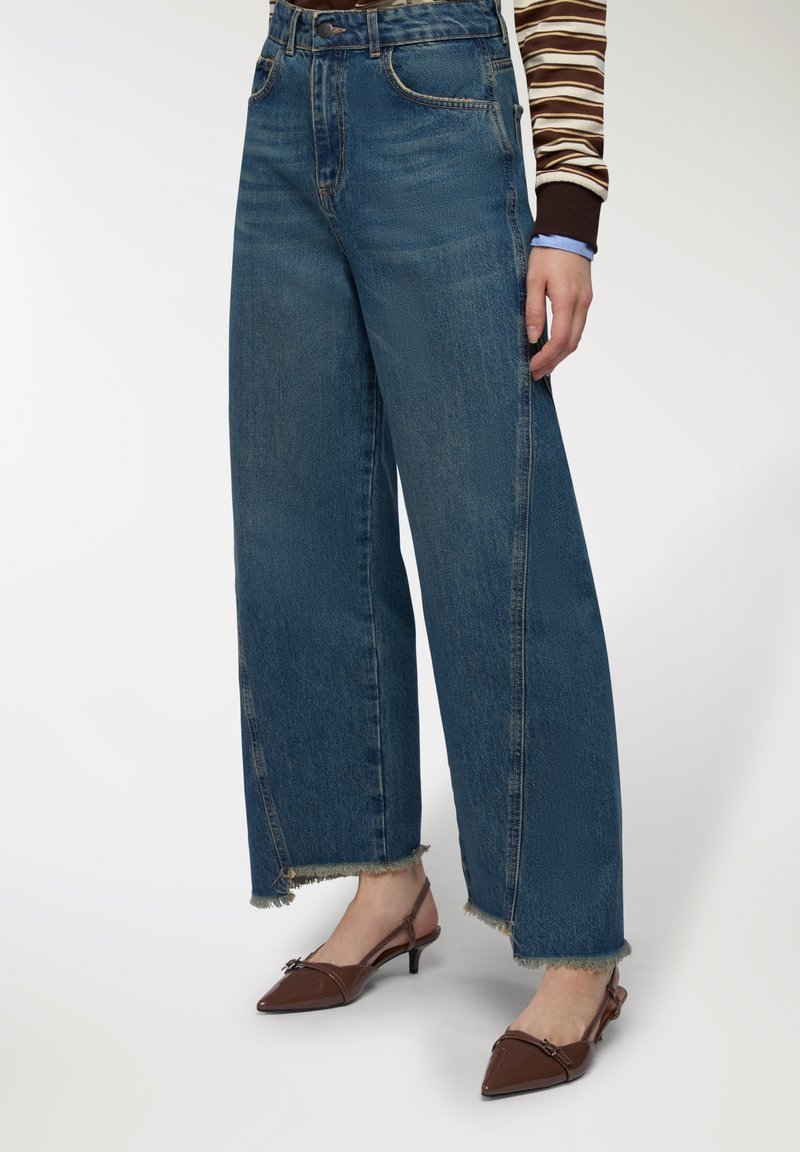 Jeans blue a gamba larga in denim, con orlo sfrangiato e leggero sbiadimento. Abbinati a tacchi slingback marroni.