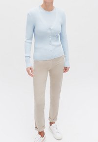Lichtblauwe geribbelde cardigan met een V-hals en knoopsluiting, gecombineerd met beige opgerolde broeken en witte sneakers. Soepele textuur.