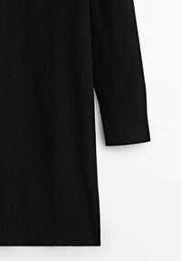 Manche d'un vêtement noir à manches longues en tricot et partie du torse sur fond blanc, montrant une texture côtelée au niveau du poignet et de l'ourlet.