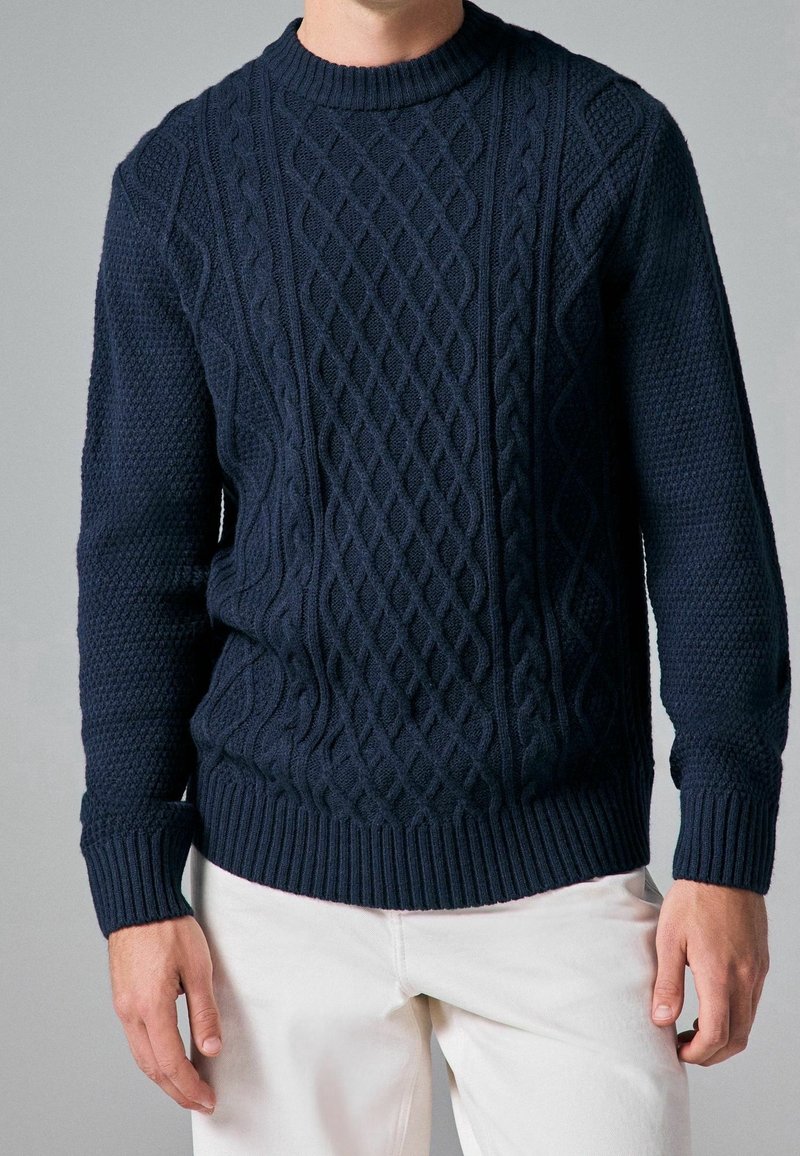 Granatowy sweter z dzianiny, z teksturowanymi wzorami w warkocze, ściągaczem przy dekolcie i mankietach oraz dopasowanym dolnym zakończeniem. Idealny na codzienne wyjścia.