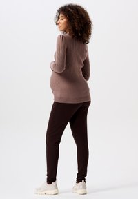 Schwangerschaftsoutfit mit einem gerippten, mauvefarbenen Pullover mit Puffärmeln und dunkelbrown Jogginghosen, kombiniert mit hellbeigen Sneakers.