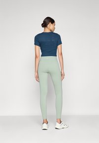 Tengerészkék, cropped póló, diszkrét logó mintával, világoszöld leggingsszel párosítva, sima textúrával és fehér sportcipőkkel.