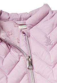 Prošívaná světle růžová bunda s vysokým límcem, zapínáním na zip a podšívkou s králičím vzorem. Obsahuje vyšívaný detail králíčka na prsou.