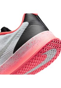 Plano aproximado de um ténis de corrida branco e preto com entressola rosa salpicada e sola exterior rosa texturizada com um logótipo swoosh branco.