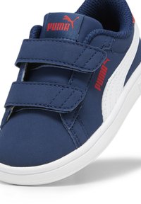Tenisi bleumarin cu benzi Velcro, partea superioară texturată, talpă din cauciuc alb și logo-ul roșu Puma pe limbă și pe lateral.