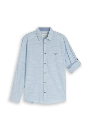 Hele sinine pika varrukaga nööbitav särk ühe rinnataskuga, metallnööpidega ja parema varruka rullitud ning nööptihvtiga kinni pandud.