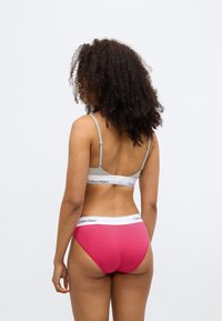 Sivá braletka s nastaviteľnými ramienkami a bielym pásom; ružové nohavičky s vysokým pásom s bielymi akcentmi, obe s logami Calvin Klein.