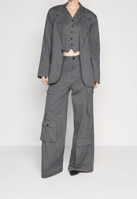 Szary trójczęściowy zestaw składający się z długiego żakietu, krótkiego kamizelki z guzikami oraz spodni cargo z szerokimi nogawkami i bocznymi kieszeniami. Materiał o teksturze klasycznego kroju.