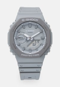 G-SHOCK watch in gray silicone with a digital and analog display, features a round face, textured accents, and water resistance up to 20 bar.