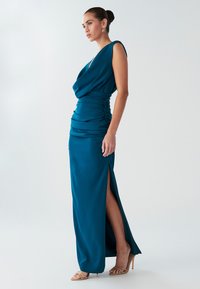 Sinine satiinist maxi-kleit lohvakalt drapeeritud kaelusega, vöökohal kortsudega ja reie kõrguse lõhikuga. Kandmisel nudetoed avatud varbaga kontsad.