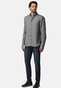 Grijze langemouwhemd met een button-down kraag en knopen aan de voorkant, gecombineerd met donkerblauwe jeans en zwarte sneakers. Soepele textuur.