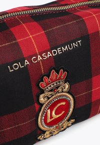 Crna i crvena karirana torbica na zip s logom u zlatnoj boji "LOLA CASADEMUNT", složenim zlatno-crvenim izvezenim grbom sa detaljom krune.