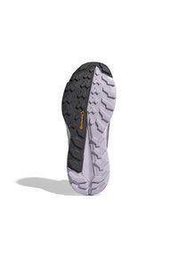 Sole běžeckých bot pro trail, s černou gumovou podrážkou a hlubokými vzorky pro dobrou přilnavost, přecházející do lila mezipodešve. Viditelné odolné materiály.