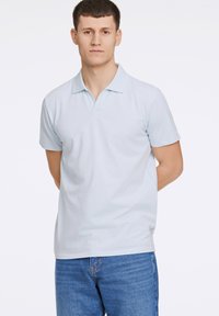 Camisa polo azul claro hecha de algodón suave, con cuello clásico y mangas cortas, combinada con jeans de mezclilla azul.