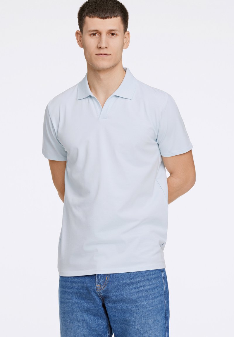 Camisa polo azul claro hecha de algodón suave, con cuello clásico y mangas cortas, combinada con jeans de mezclilla azul.