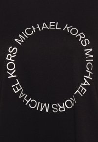 Camiseta de algodón negra con un diseño circular en el que está impreso "MICHAEL KORS" en plateado. Textura suave, escote redondo.