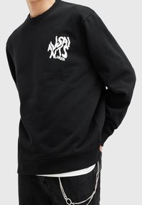 Black sweatshirt in cotton blend features a distorted white logo on the chest, crew neckline, and ribbed cuffs with a relaxed fit.