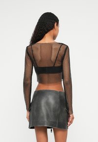 Svart mesh langermet crop topp med rund halslinje, kombinert med et grått lær mini-skjørt med bakglidelås og sidelommer.