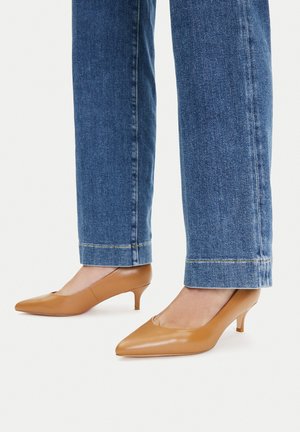 Brązowe skórzane buty na niskim obcasie typu kitten heel z ostrym noskiem i wycięciami, noszone z niebieskimi dżinsami o prostych nogawkach z podwiniętym dołem.