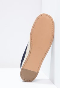 Marinblå tygskor med en strukturerad jute-liknande sula. Yttersulan är beige med en slät yta, med minimal sömnad och varumärkeslogotyp.