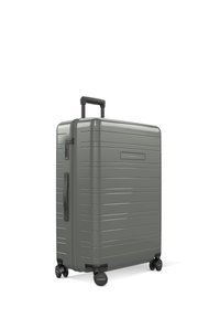 Valise à coque rigide de couleur gris mat avec texture rainurée, poignée extensible, poignée latérale et quatre roues pivotantes. Design compact pour les voyages.