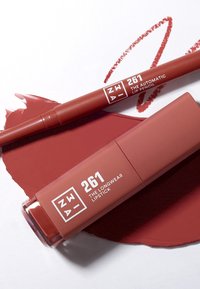 Långvarigt läppstift och automatisk läpppenna i en matt röd nyans. Tuben och pennan har vit branding. Röd läppstiftsprov under.