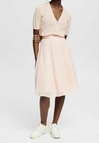 Lyse ferskenfarvet cardigan med korte ærmer og to knapper kombineret med et flydende, knælængde chiffon skørt i en lignende nuance og hvide sneakers.