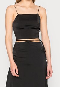 Top nero in satin, corto, con spalline sottili, scollo quadrato e dettaglio in vita annodato, caratterizzato da una texture liscia e un design aderente.