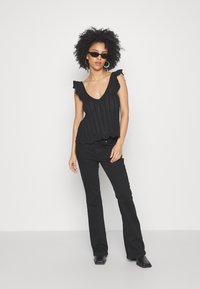 Svart ärmlös topp med volangdetaljer på axlarna, med en djup V-ringning och strukturerad stickad design. Kombinerad med svarta utsvängda jeans och klackskor med blockhäng.