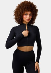 Black cropped athletic zip-up jacket with long sleeves and ribbed texture, paired with high-waisted black leggings. Smooth, fitted design.