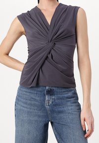 Haut sans manches gris foncé avec un nœud torsadé, associé à un jean en denim bleu taille haute porté par une personne.