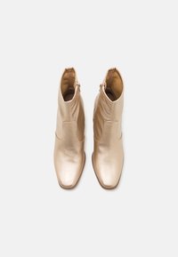 Bottines dorées en cuir lisse, avec bout carré et fermeture éclair latérale, présentant une coupe ajustée et un léger talon.