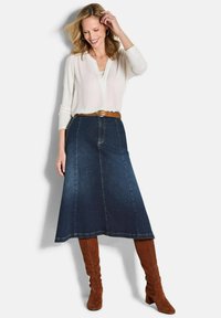 Jupe en denim A-line bleu foncé avec des coutures contrastantes, associée à un haut léger à manches longues et des bottes en suede marron jusqu'au genou.