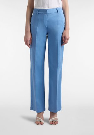 Pantaloni azzurri chiaro, a vita alta, a gamba larga, realizzati in tessuto liscio con pieghe frontali; abbinati a sandali bianchi con cinturini.