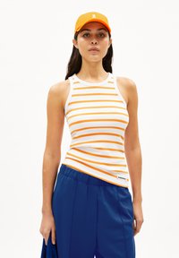 Weißes Tanktop mit orangefarbenen Streifen, gerippter Textur und Rundhalsausschnitt; kombiniert mit blauen Pants mit elastischem Bund; orangefarbene Kappe mit Logo.
