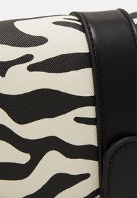 Zebramønstret taske med en struktureret lys cremefarvet bund og sorte striber, suppleret med sorte læderdetaljer og lukninger.