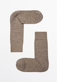 Brune strikkede sokker med ribbede manchetter, glat tekstur og rund tå. Arrangeret i en abstrakt form. Har et konsistent, subtilt mønster.