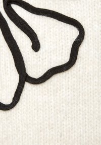 Weißer gestrickter Stoff mit einem markanten schwarzen, strukturierten Rand, der eine abstrakte Form bildet. Die Oberfläche zeigt leichte Fasern und Weichheit.