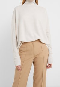 Pull à col roulé crème avec une coupe décontractée, des manches larges et une texture côtelée, associé à un pantalon fluide beige taille haute.