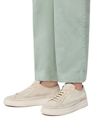 Baskets en suède beige avec des détails perforés, bout rond et épaisse semelle en caoutchouc blanche, associées à un pantalon en corduroy vert clair.