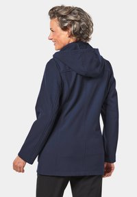 Marineblaue Kapuzenjacke mit langen Ärmeln, taillierter Silhouette, sichtbaren Nähten und glatter Stoffoberfläche. Versteckte Fronttaschen.