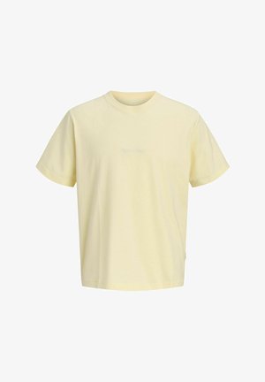 Junge in gelbem kurzärmligem Hemd, knielangen Jeansshorts, weißen Socken und beigen Schnürschuhen steht und schaut zur Seite.