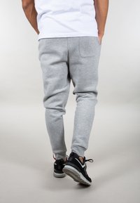 Graue Jogginghosen mit schmaler Passform, aus weichem Material, mit seitlichen Taschen und gerippten Bündchen. Kombiniert mit schwarzen Sportschuhen.