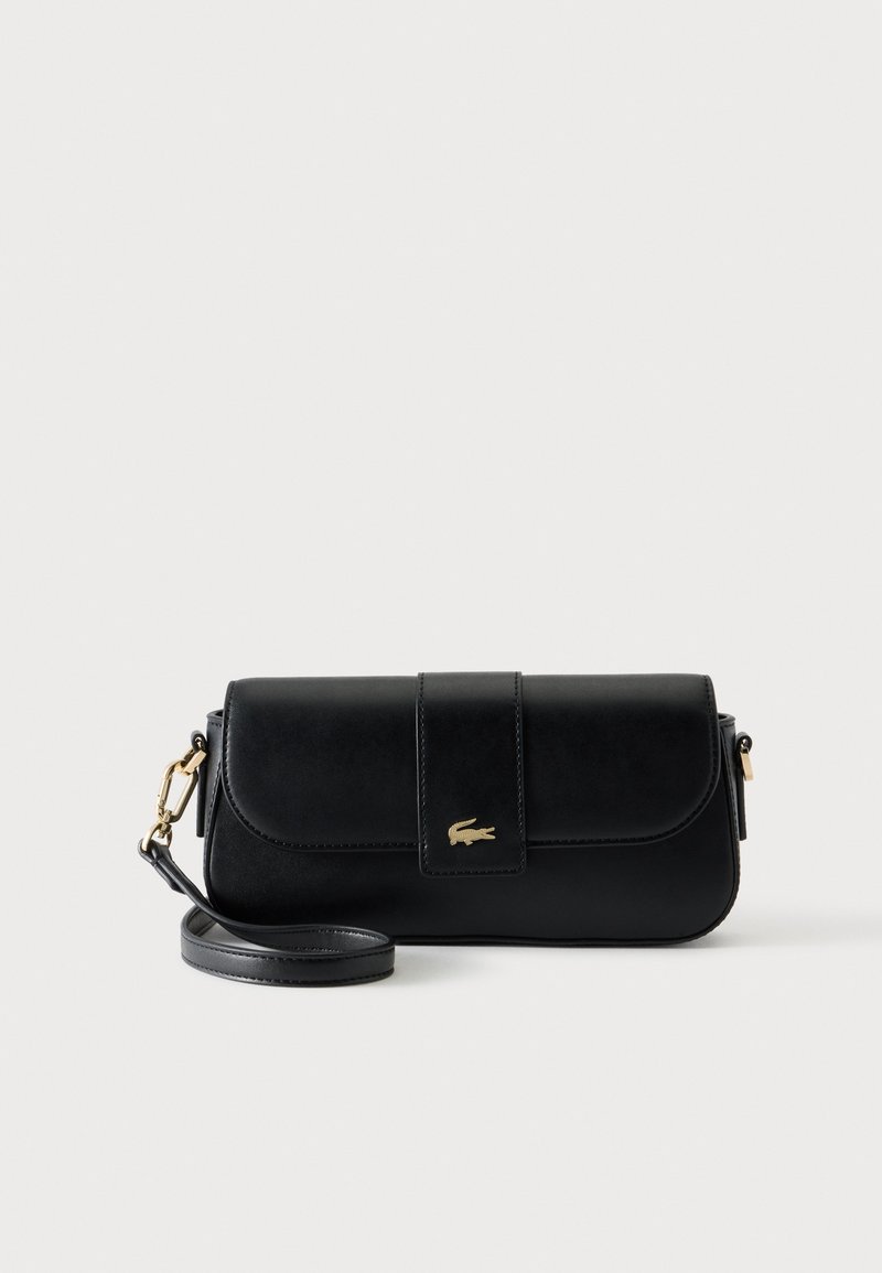 Sac d'épaule en cuir noir avec fermoir doré et petit logo crocodile doré sur le rabat avant, bandoulière amovible enroulée à côté.