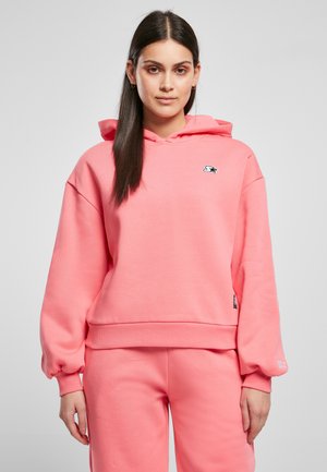 Haut en coton rose à capuche avec une coupe décontractée, des poignets côtelés et une poche kangourou. Présente un petit logo sur la poitrine et une texture douce.