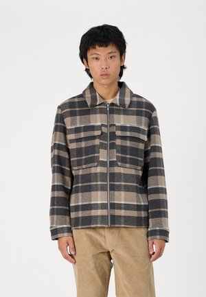 Plaid jacket in black, beige, and gray hues; full zip, collar, and two chest pockets. Made of textured fabric with a soft finish.